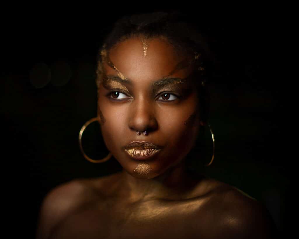 model with gold makeup and earrings in front of black background