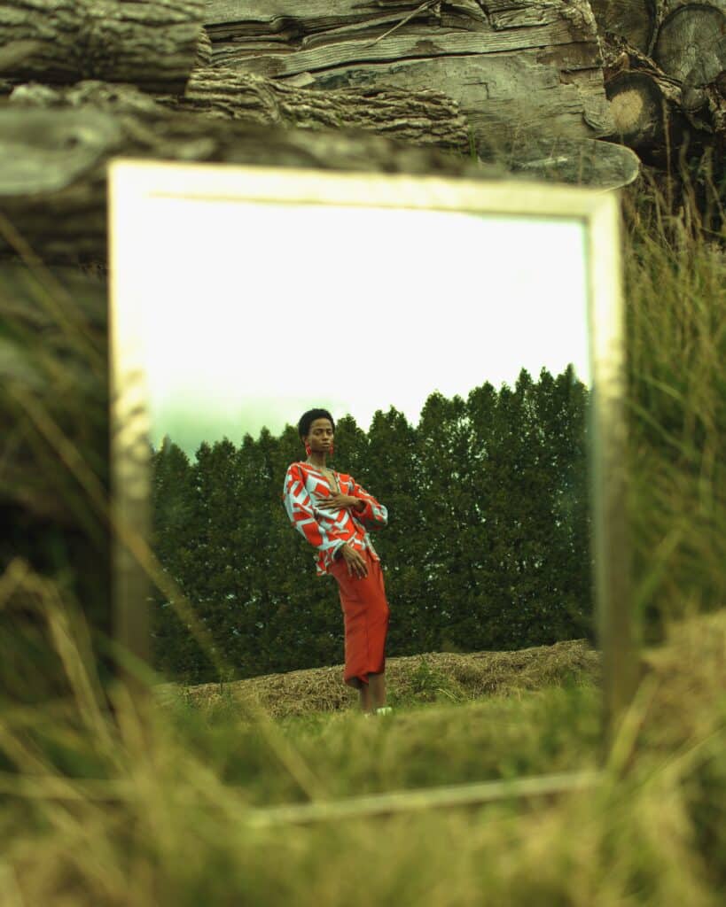 Pessoa posando no campo, refletida em um espelho ao lado de um muro de pedra