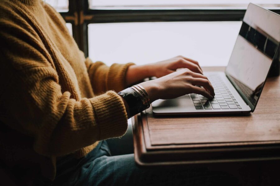 person wearing yellow sweater typing on a laptop at a table scaled e1697488121770