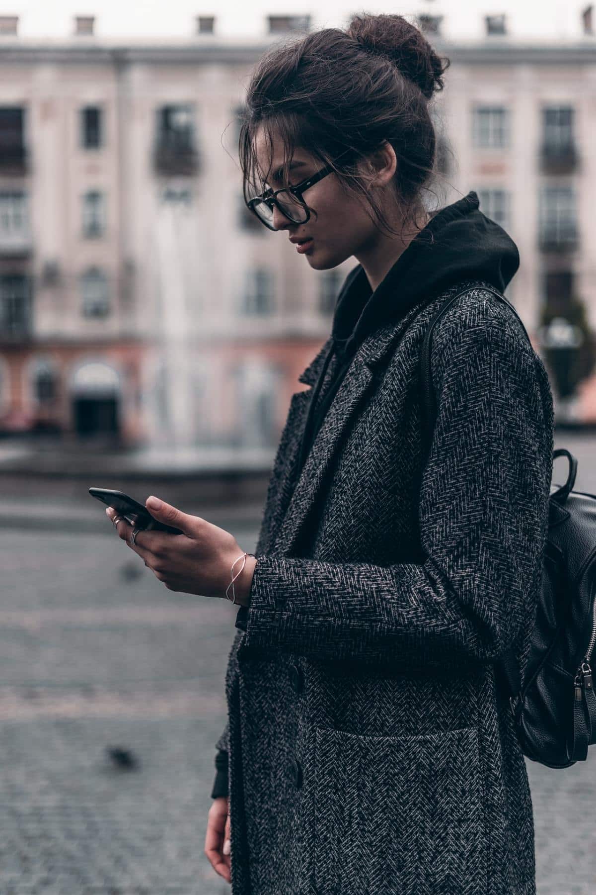 Femme en veste gris foncé regardant son smartphone