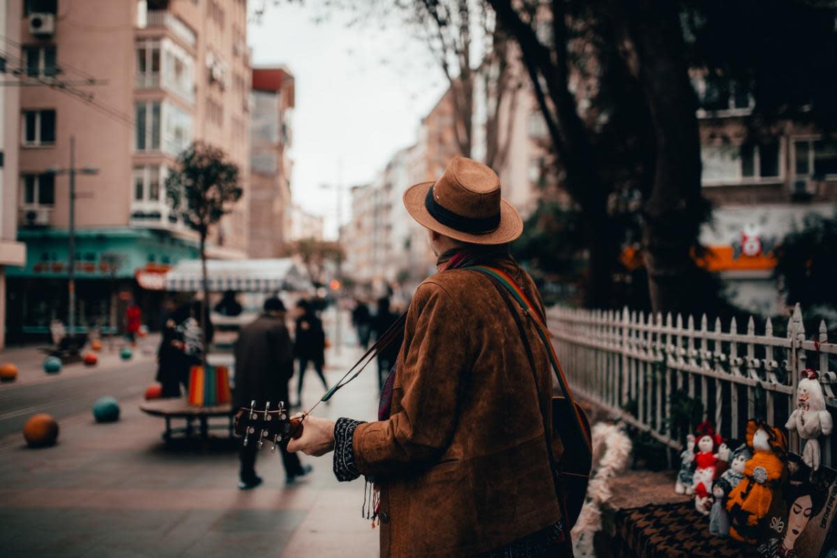 homme avec chapeau et veste marron jouant de la guitare