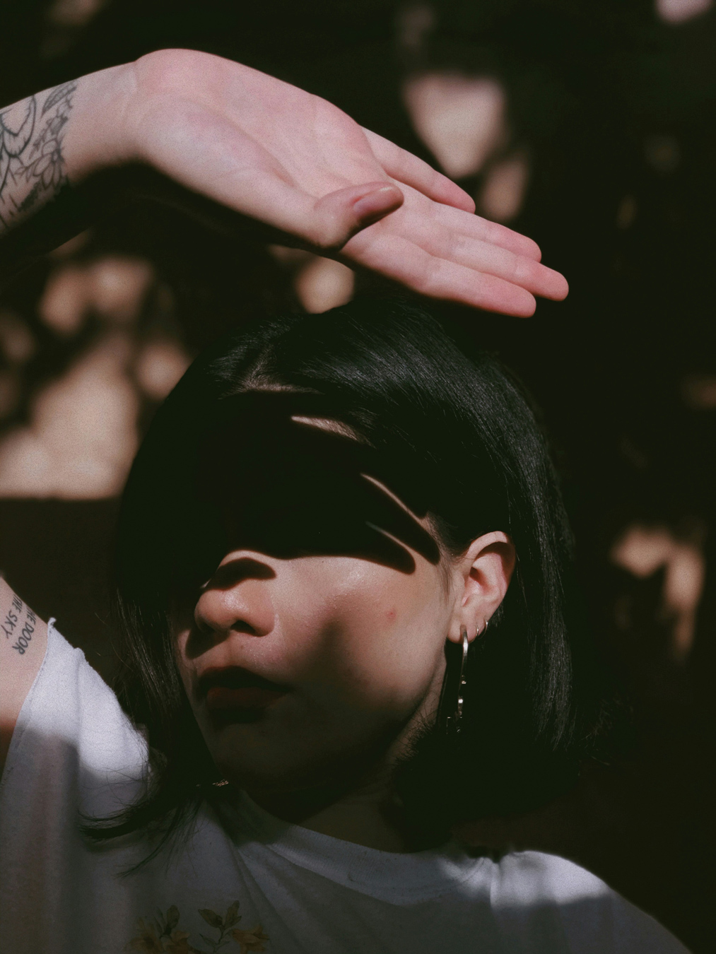 portrait of woman with short dark hair and her hand over her head causing a shadow across her eyes