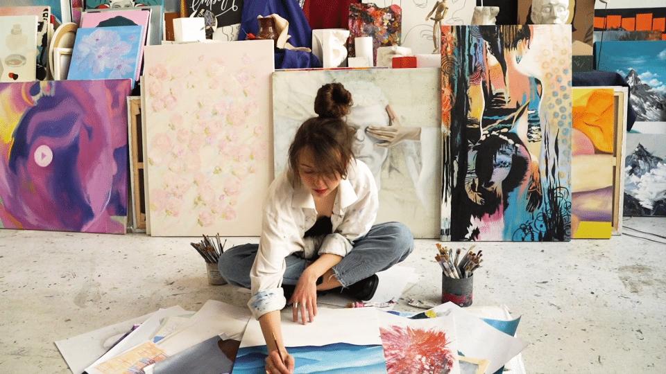 mujer sentada en el suelo de su estudio, pintando sobre un lienzo frente a ella