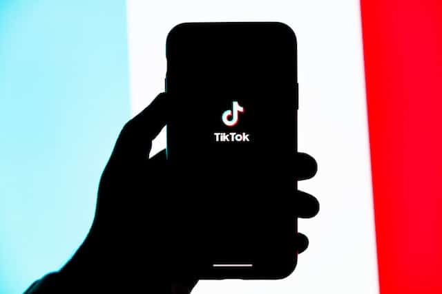 silhouette d'une main tenant un téléphone. L'écran du téléphone affiche le logo TikTok.