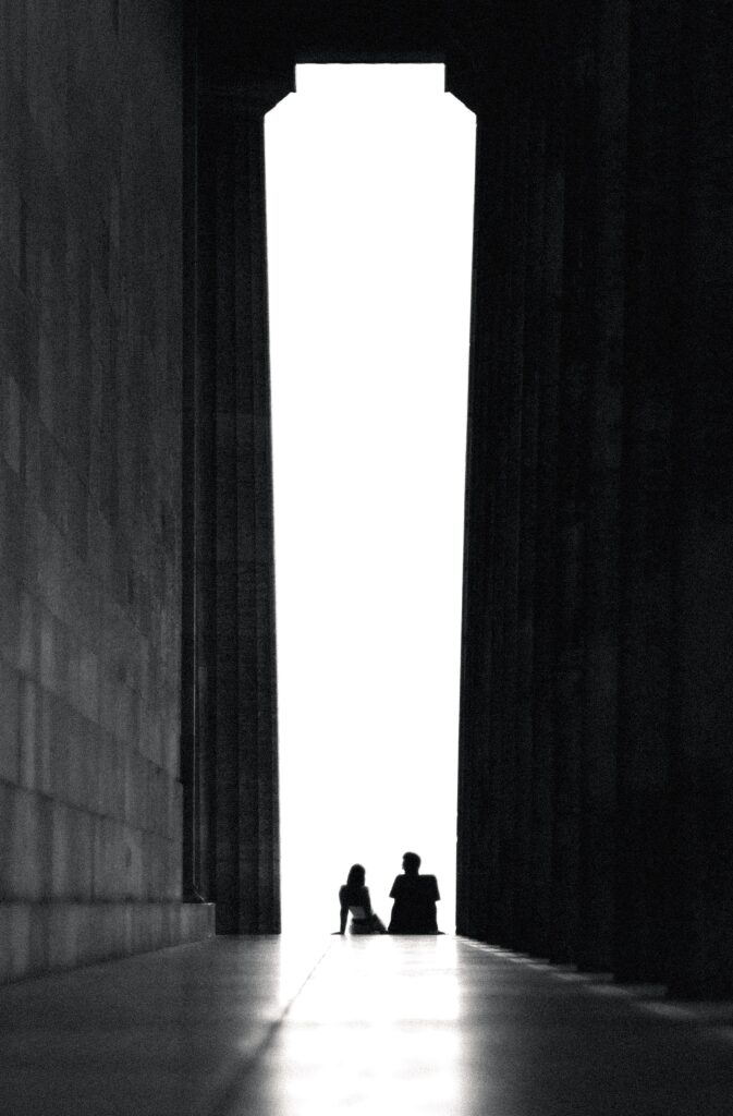 two people sitting on the floor at the entrance to a tall hallway