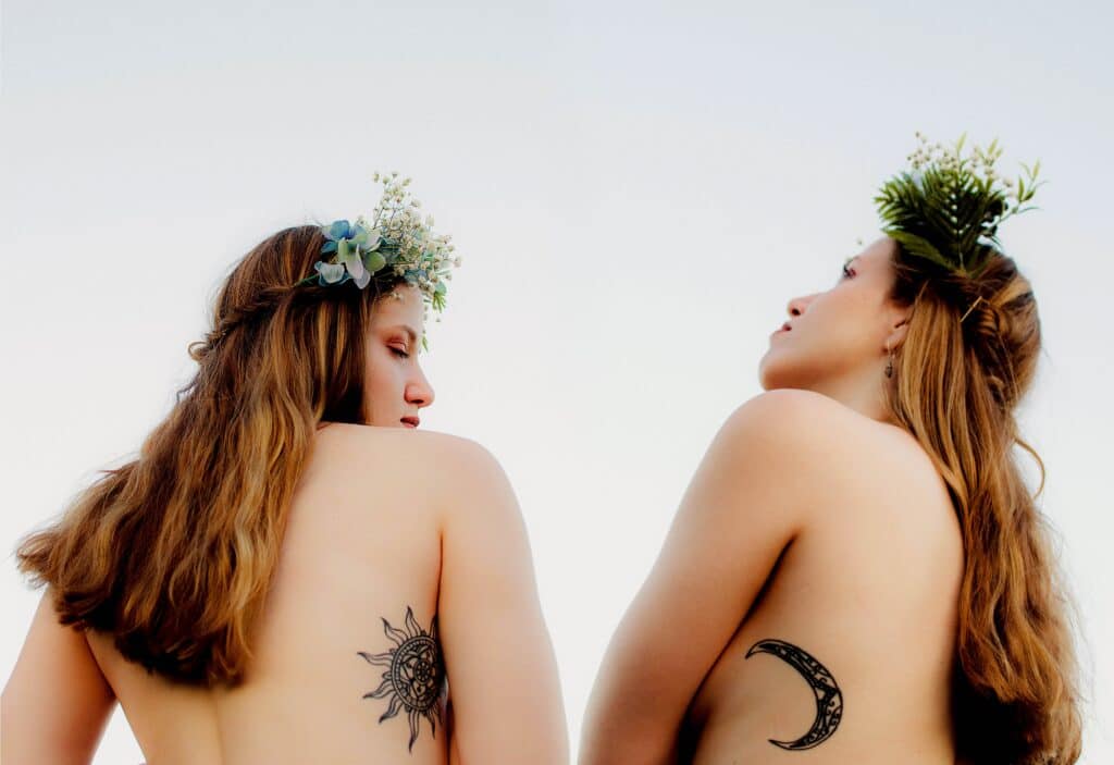 dos mujeres con coronas de flores y tatuajes de un sol y una luna