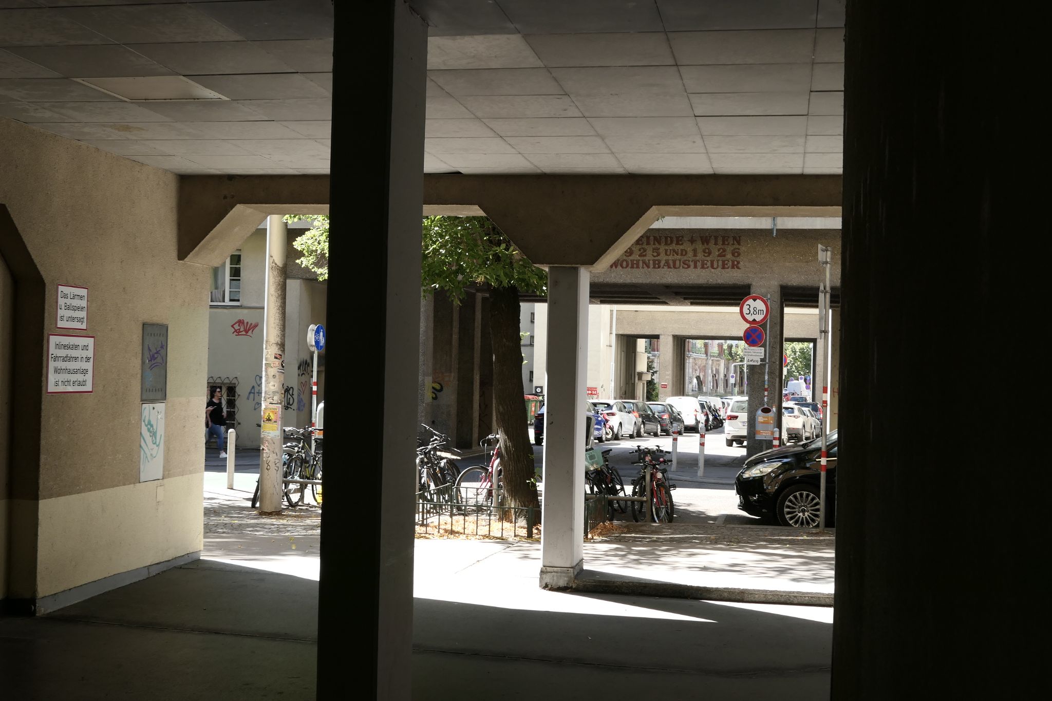Covered arcade in a historic Vienna housing complex overlooking a street with bicycles and parked cars.