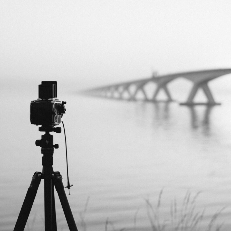 câmera vintage em tripé ao lado de ponte e água durante neblina em escala e1693940551804