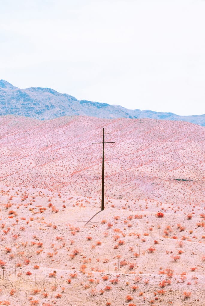 pink-toned desert landscape with a single electric pole in the center and blue mountains in the distance