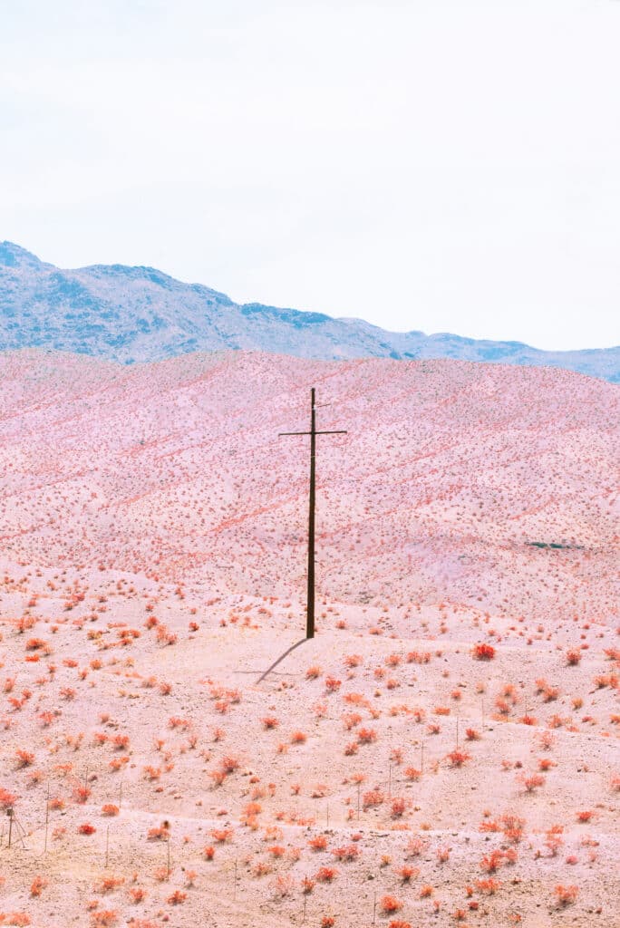 Paisagem desértica em tons de rosa com um único poste elétrico no centro e montanhas azuis à distância