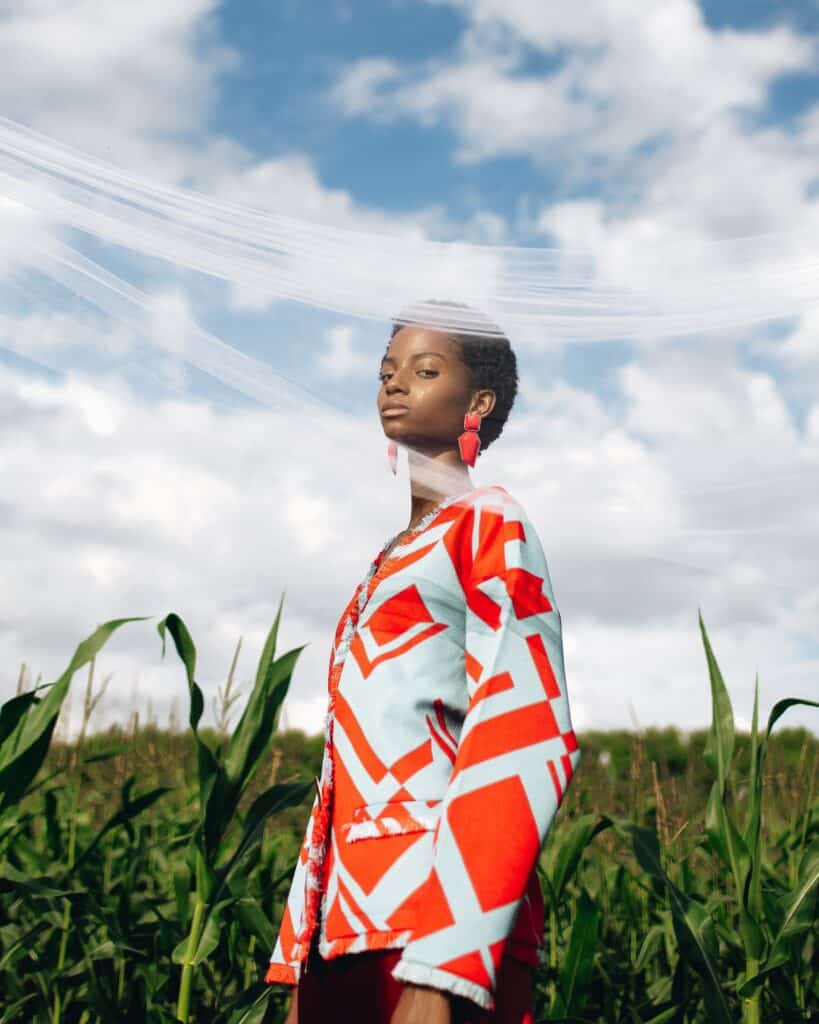 femme vêtue d'une veste à motifs audacieux, debout dans un champ de jeunes plants de maïs