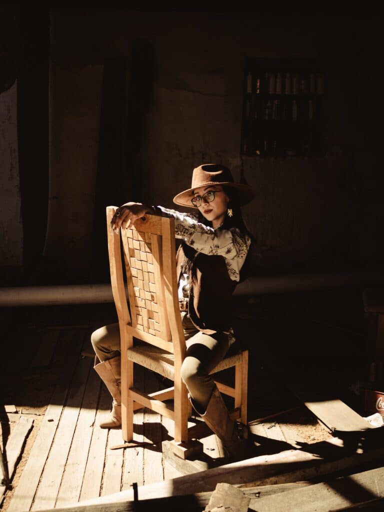woman in coat and felt hat sitting in a chair backward in a patch of sunlight
