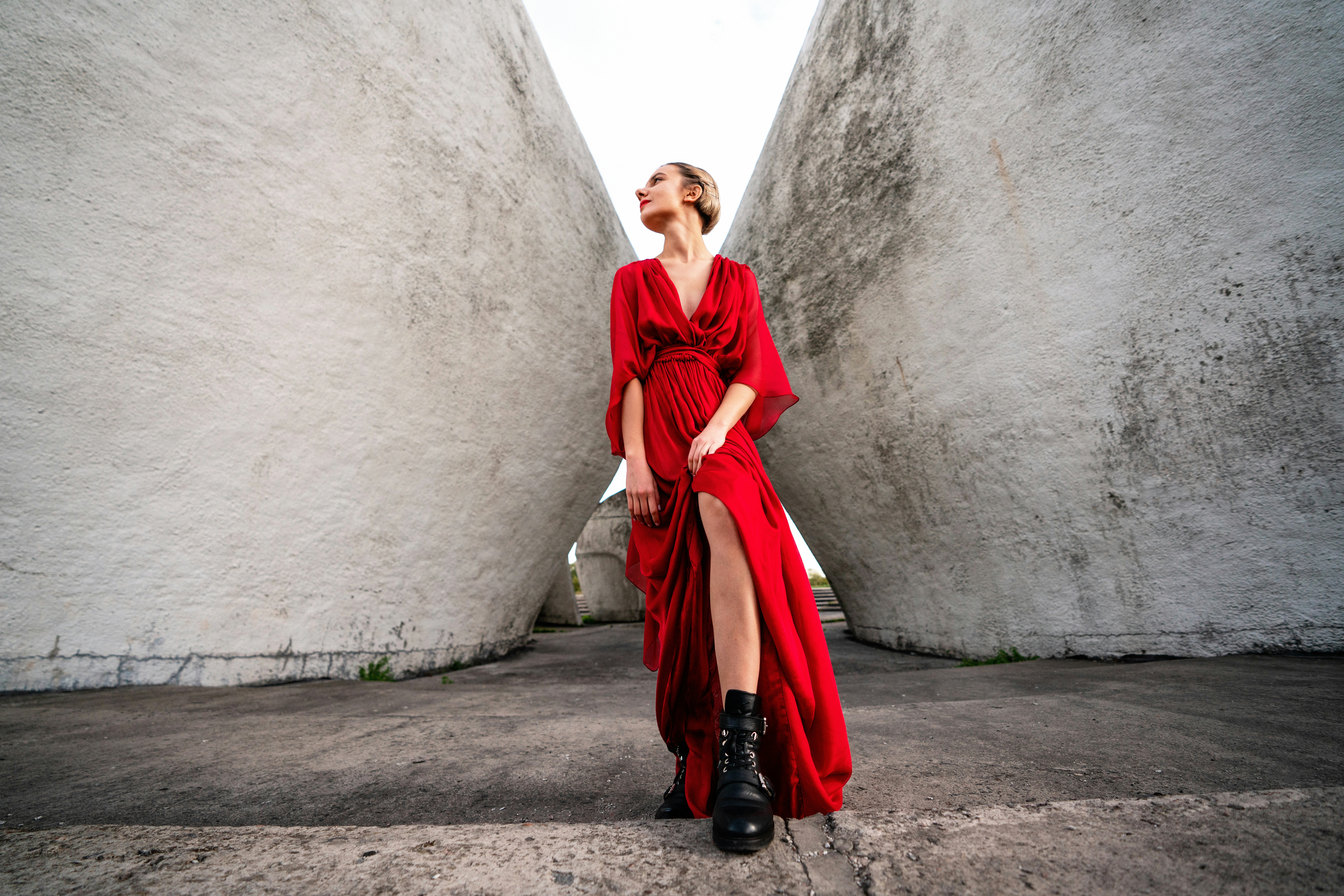 mujer con vestido rojo y botas negras de pie entre muros de hormigón
