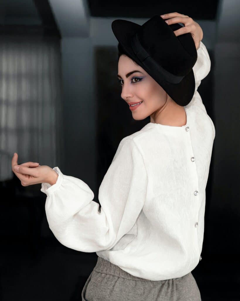 mujer con blusa blanca y sombrero usando las manos al posar