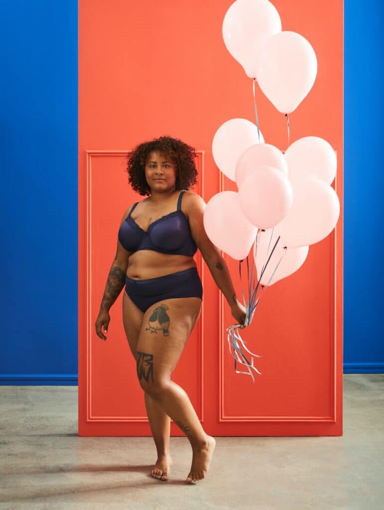 woman posing with weight on one leg wearing black underwear and holding balloons