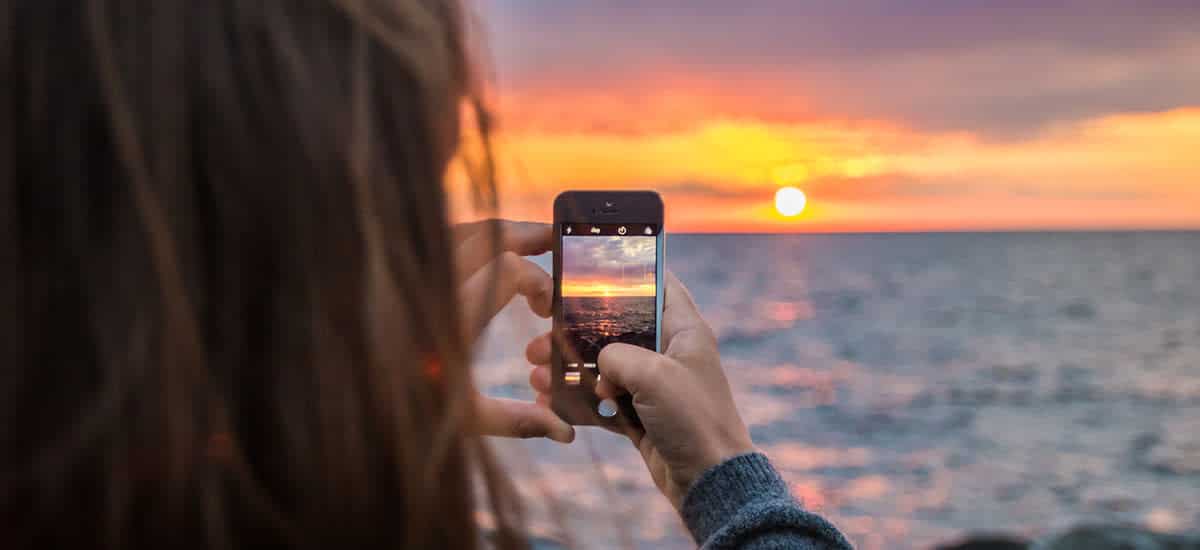 femme prenant une photo du coucher de soleil avec un téléphone-caméra