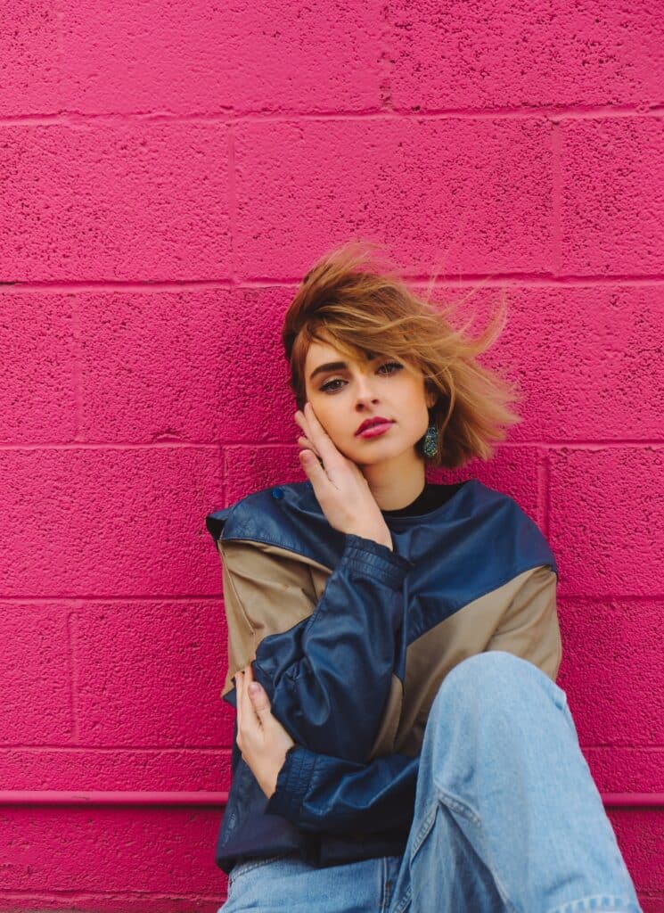 mujer con chaqueta azul marino y topo sentada junto a una pared rosa intenso