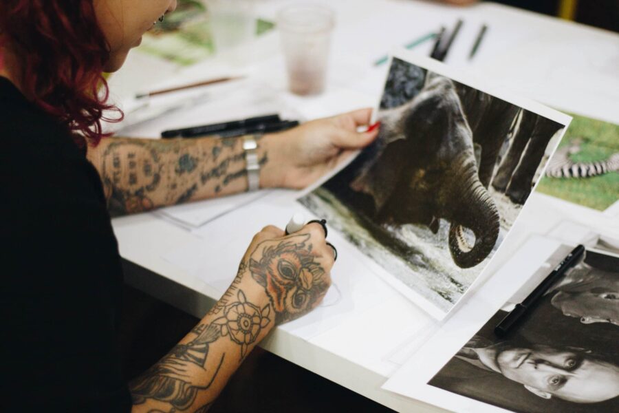 femme aux bras tatoués tenant un tirage photo d'un éléphant à l'échelle e1698299272433