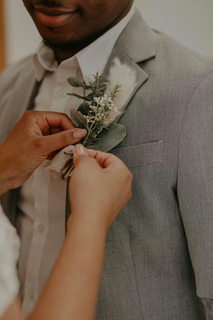 Mãos de mulher prendendo uma flor na lapela do noivo